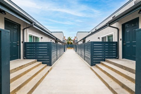 a corridor between two buildings with stairs and blue doors