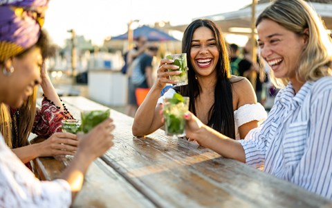 Four people are sitting at a table, laughing and enjoying drinks.