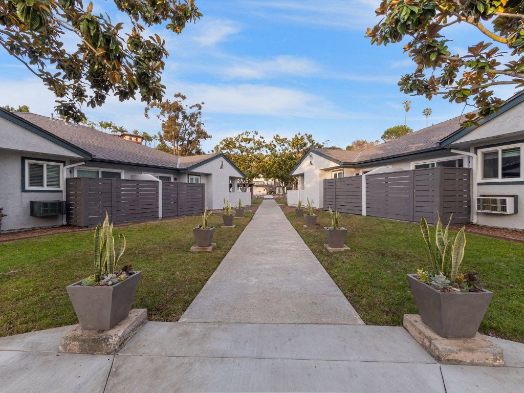 a pathway between two rows of white houses with plants in pots
