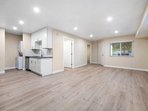 an empty living room with a kitchen and a window