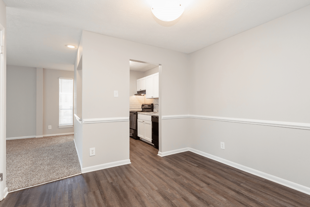 an empty living room and kitchen with white walls and wood flooring at The Hudson, Fayetteville, NC