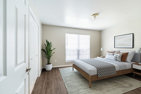A bedroom with a bed, a plant, and a framed picture on the wall.