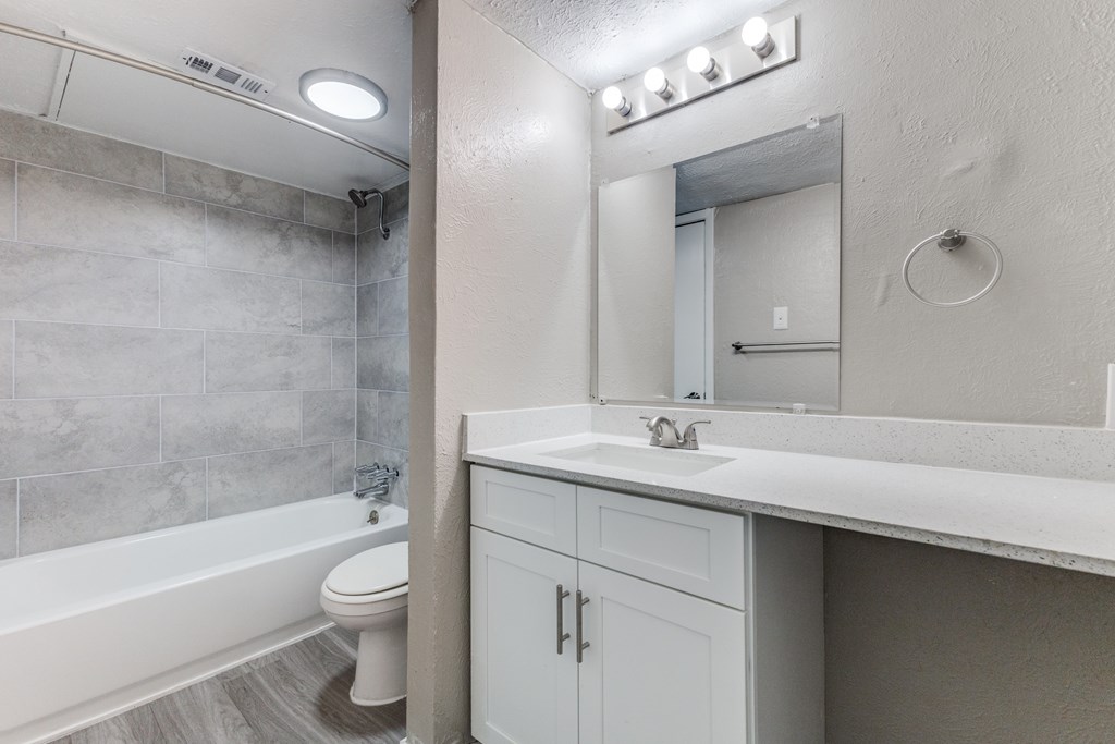 A bathroom with a white tub, sink, and a mirror with lights above it.