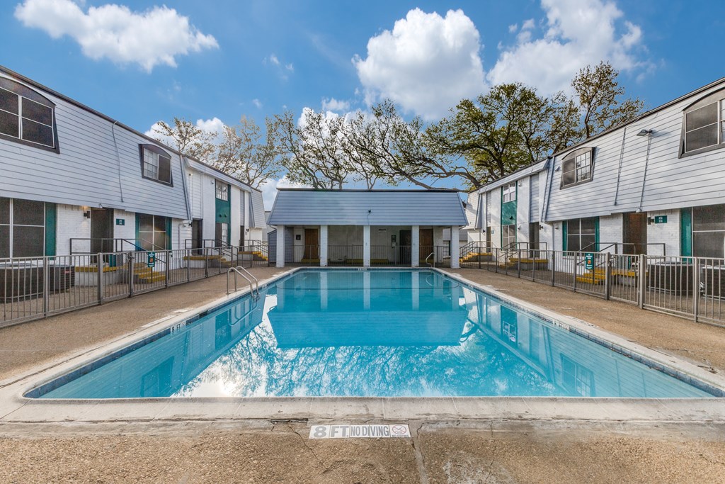 A swimming pool in front of a building with a blue sky and clouds in the background.