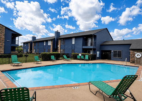 A swimming pool surrounded by green chairs and a building in the background.