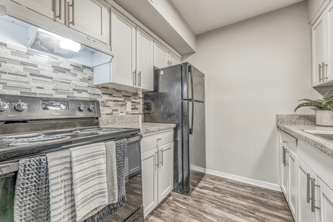 A kitchen with a black refrigerator and a stone backsplash.