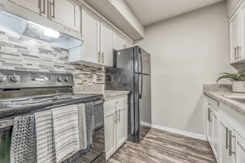 A kitchen with a black refrigerator and a stone backsplash.