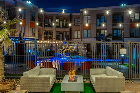 Outdoor fire pit lounge with pool and string lights at The Watson Apartments, Grand Prairie, TX