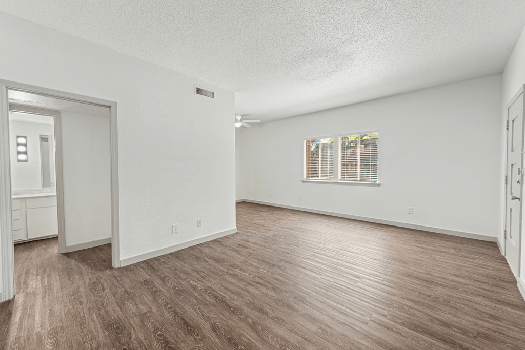 a spacious living room with white walls and wood flooring