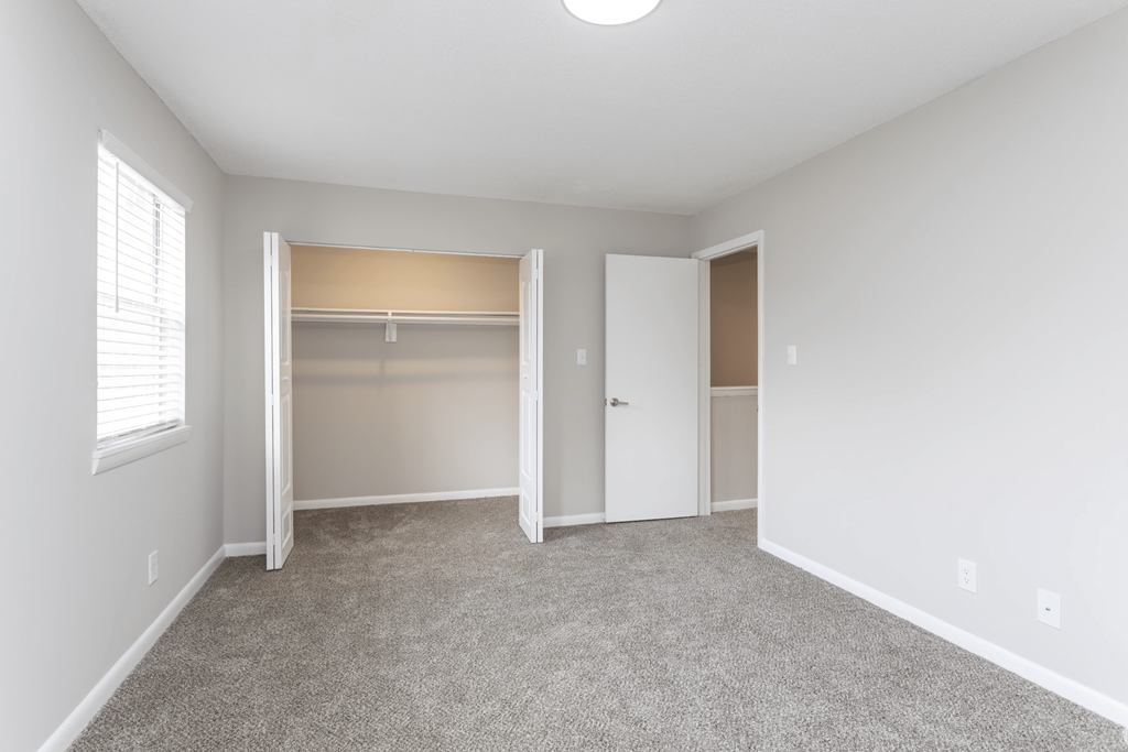 A room with a carpeted floor and a window with blinds.