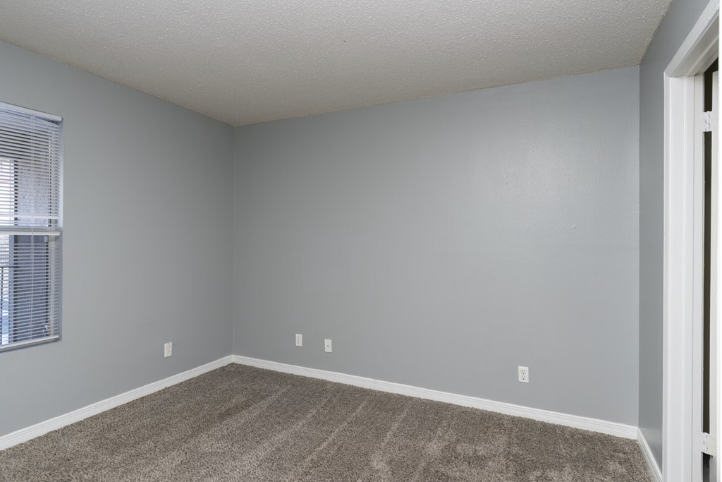 A room with a carpeted floor and a window with blinds.