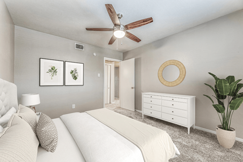 A bedroom with a white bed, a white dresser, and a ceiling fan.