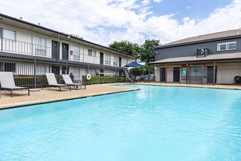 A swimming pool in front of a building with lounge chairs around it.