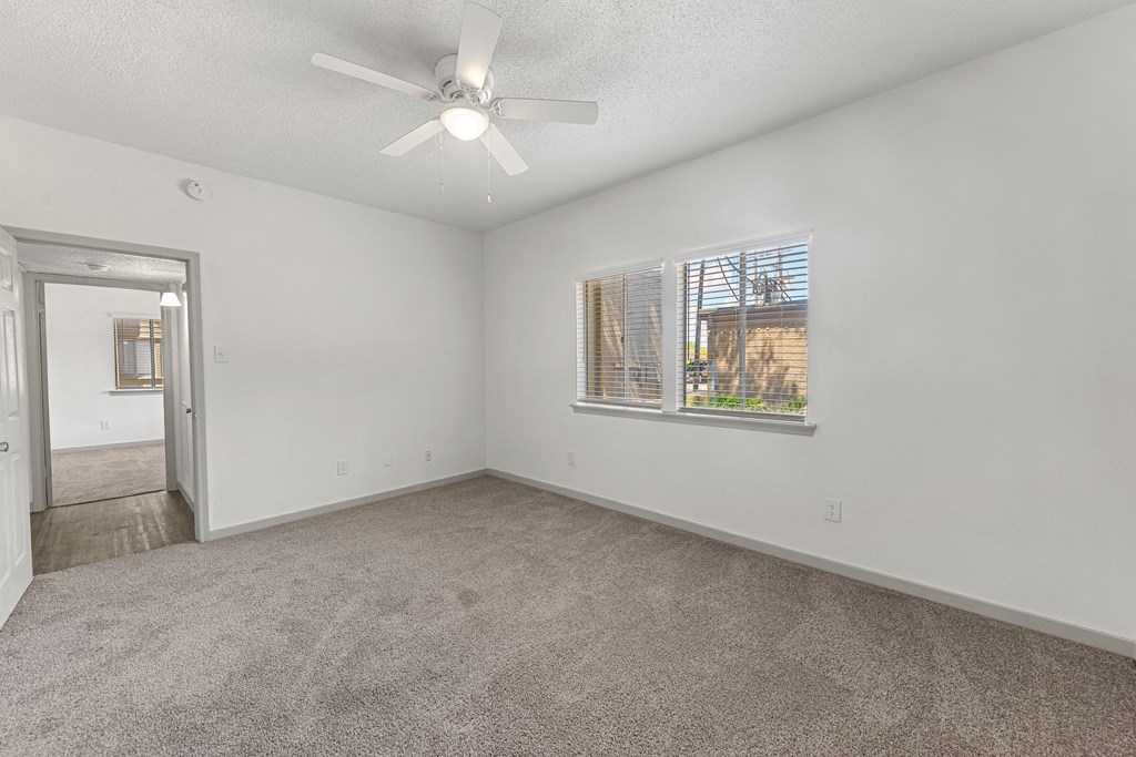 an empty living room with a window and a ceiling fan