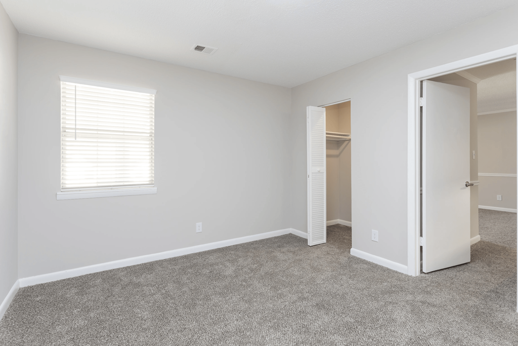 A room with a carpeted floor and a window with blinds.