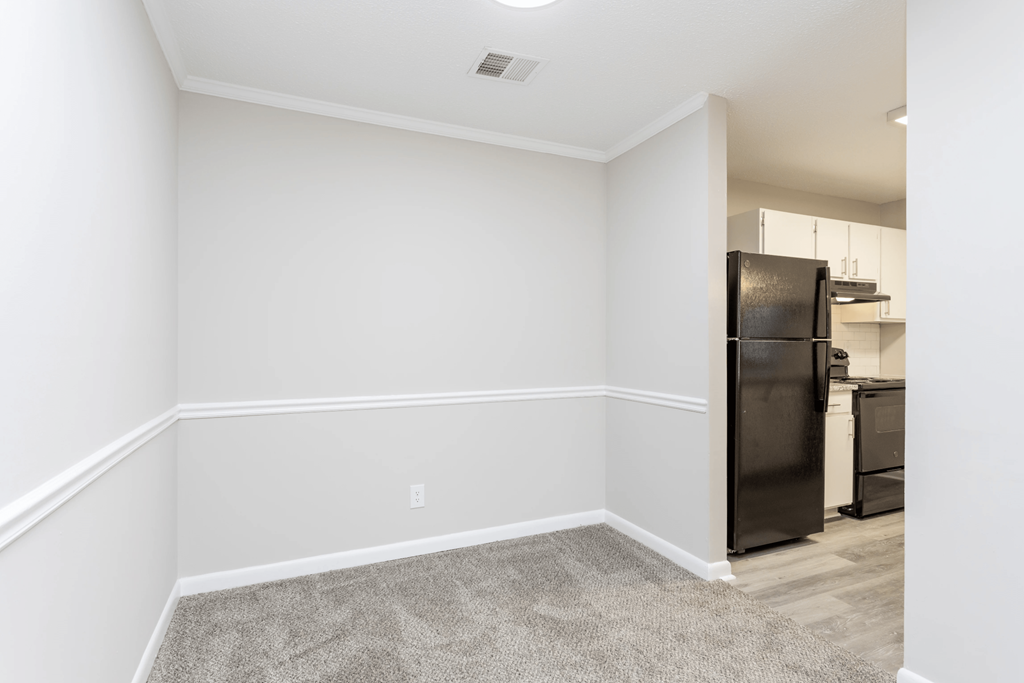 A kitchen area with a black refrigerator and a white wall.