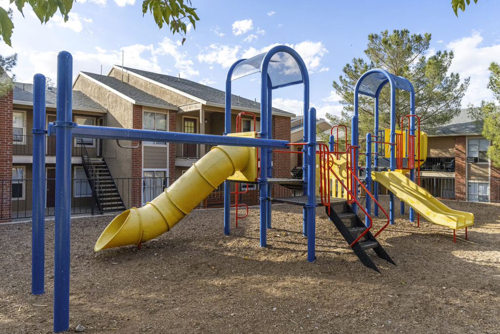 A playground with a yellow slide and a blue and red swing set.
