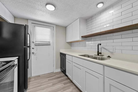 A kitchen with white cabinets and a black refrigerator.