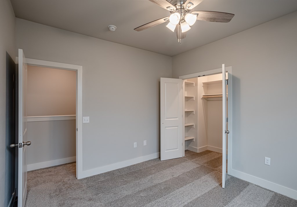 A room with a ceiling fan and two open doors at Cedar Crest Apartments, Farmington 72730