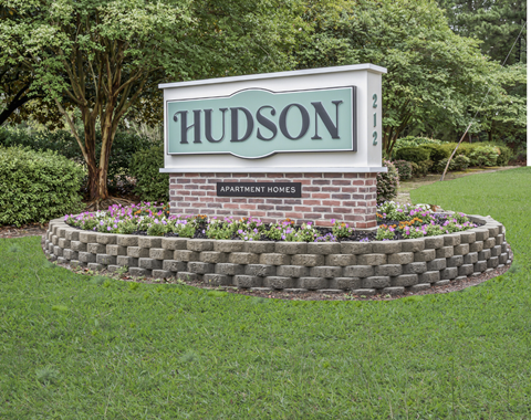 The sign for Hudson Apartments in a grass field and trees