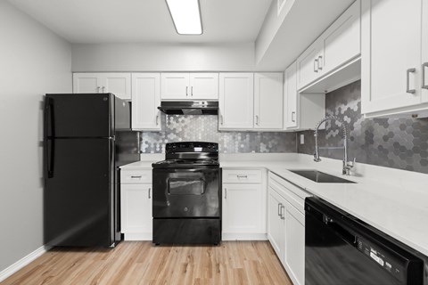 A black refrigerator is in a kitchen with white cabinets.