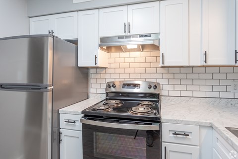 A modern kitchen with a stainless steel refrigerator, a stove with an oven, and white cabinets.