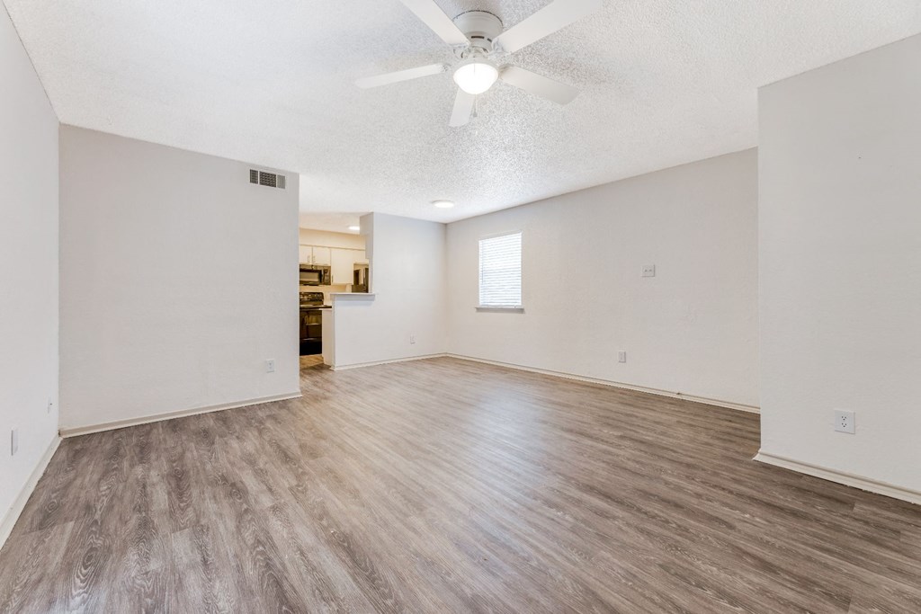 an empty living room with a ceiling fan and a kitchen