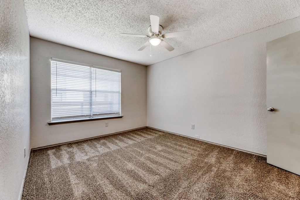 an empty bedroom with a ceiling fan and a window