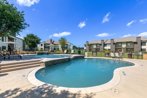 A swimming pool surrounded by a concrete patio and a grassy area with trees.
