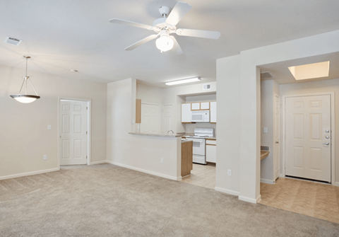 A spacious room with a ceiling fan and a kitchen area in the background.