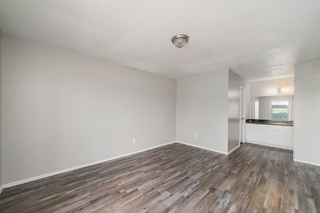 an empty living room with wood flooring and a kitchen at Helios, Dallas, TX 75240