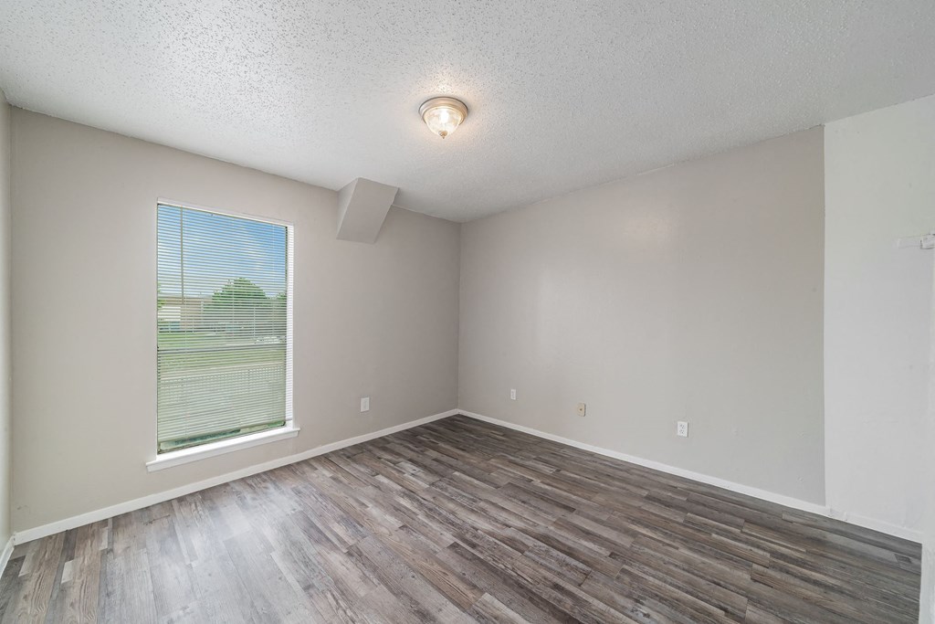 an empty living room with wood flooring and a large window an empty living room with wood flooring and a large window at Helios, Dallas, 75240