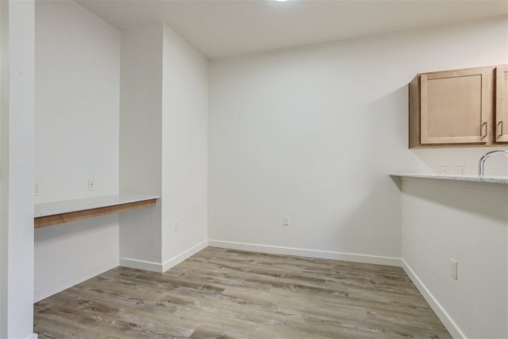 an empty room with wood flooring and a kitchen