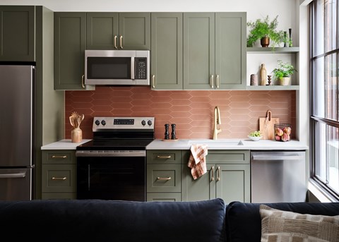 A kitchen with green cabinets and a brick backsplash.