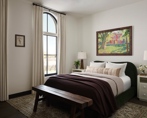 A bedroom with a large bed, a bench, and a painting on the wall.