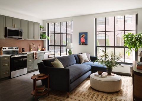 A modern living room with a blue couch and a kitchen area with a microwave and oven.