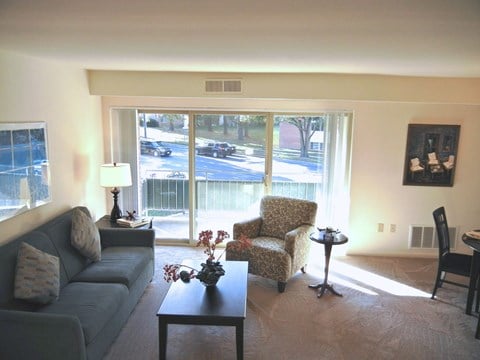 A living room with a couch, chair, and a table with a vase of flowers on it.