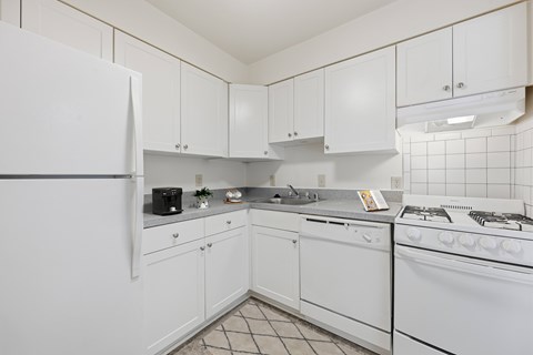 A white kitchen with a refrigerator, stove, and cabinets.
