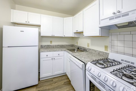A white kitchen with a stove, sink, and cabinets.