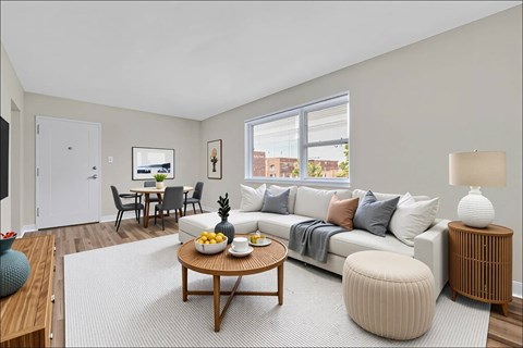 A living room with a white couch, a wooden coffee table, and a grey ottoman.