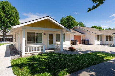 a white bungalow with a porch and a sidewalk in front of a house