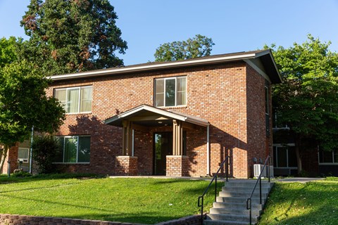 the front of a brick house with a lawn and steps