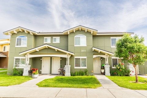 a green house with a lawn and a tree in front of it