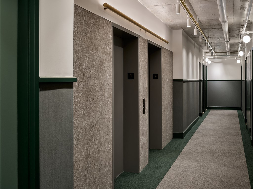 a row of elevators in a hallway with concrete walls and green carpet
