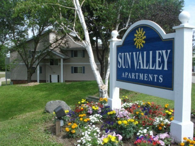 a sign that says sun valley apartments with a bunch of flowers in front of it