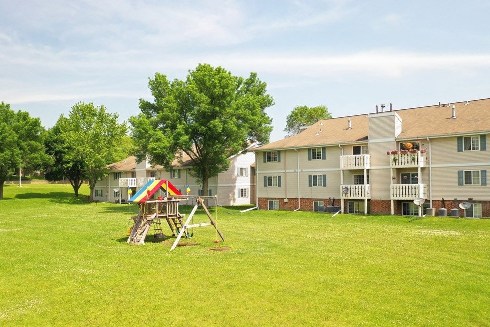 a playground sits in the middle of a grassy area in front of an apartment complex