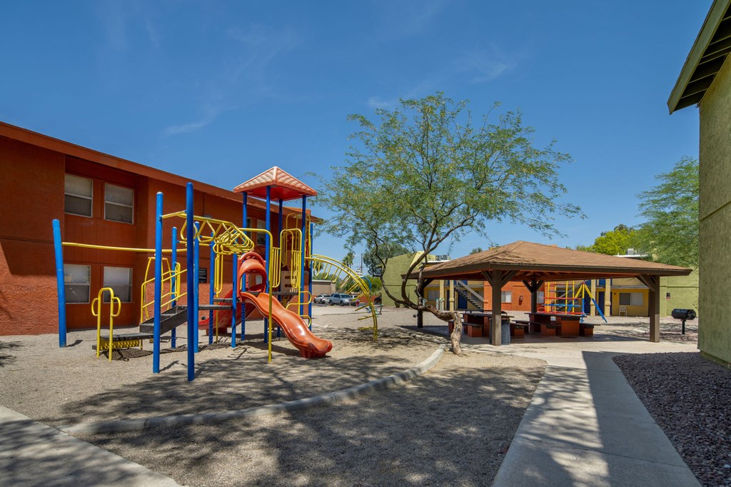 A playground with a yellow slide and a brown pavilion.