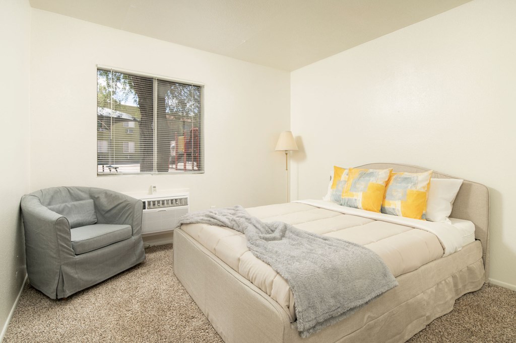 A bedroom with a bed, chair, and window.