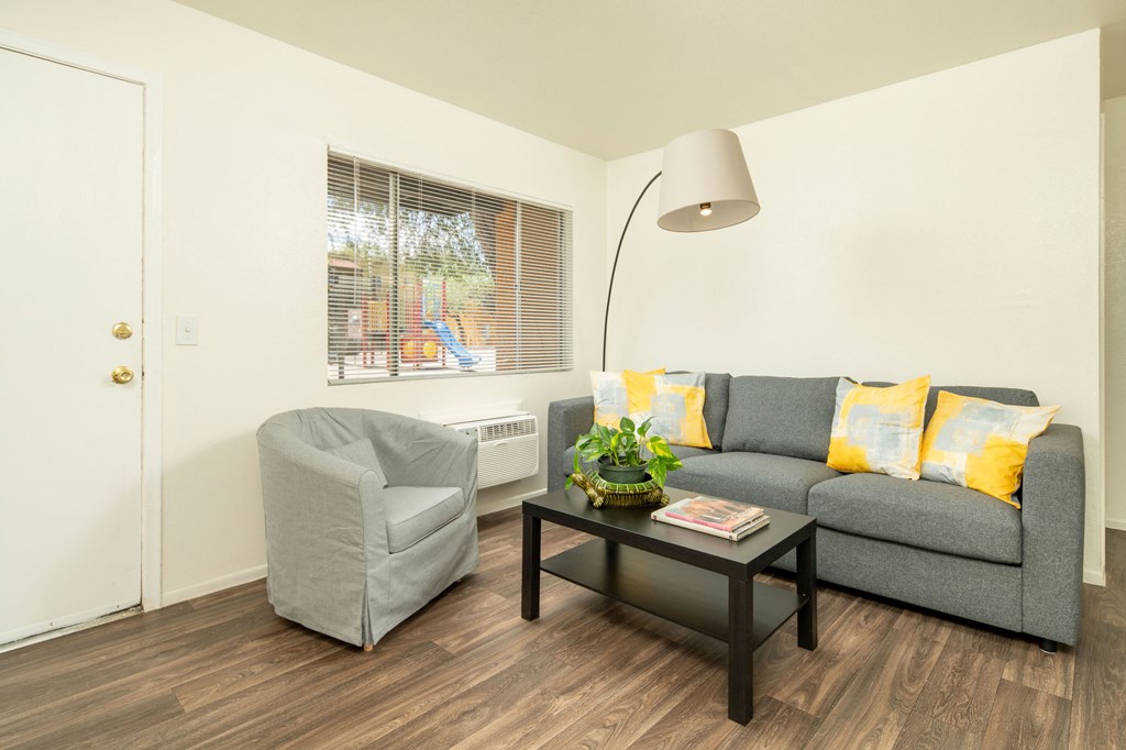 A grey couch with yellow pillows sits in a living room with a grey armchair and a coffee table.