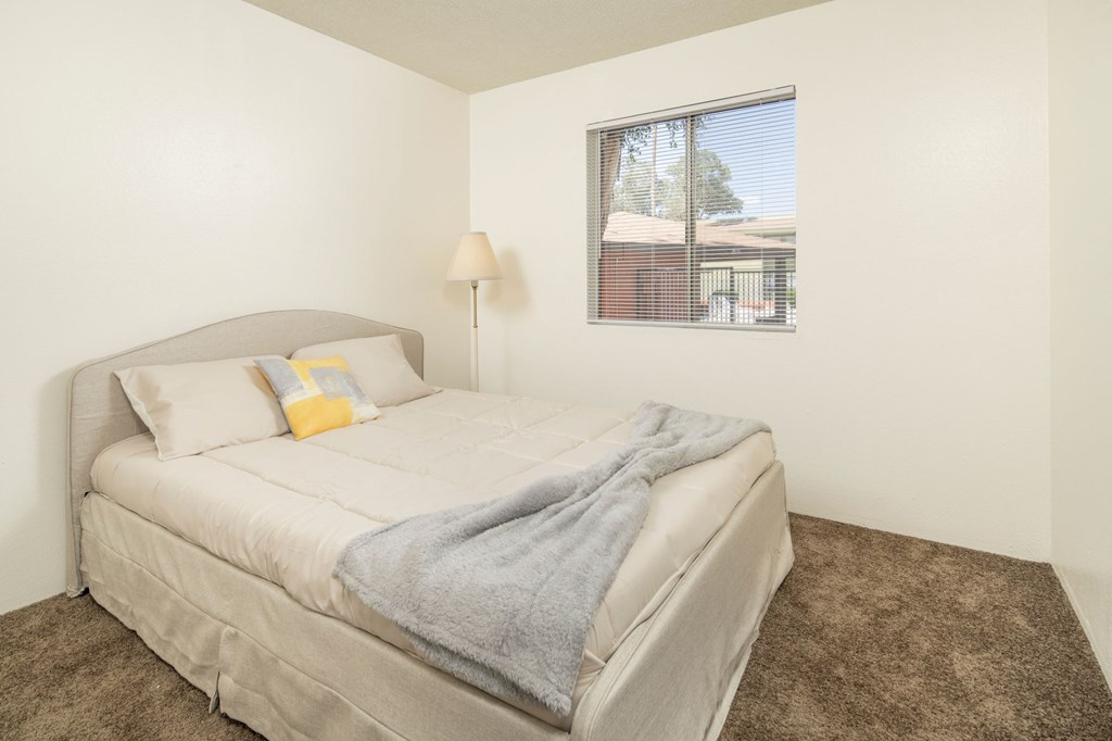 A bedroom with a bed, pillows, a blanket, a lamp, and a picture of a house on the wall.